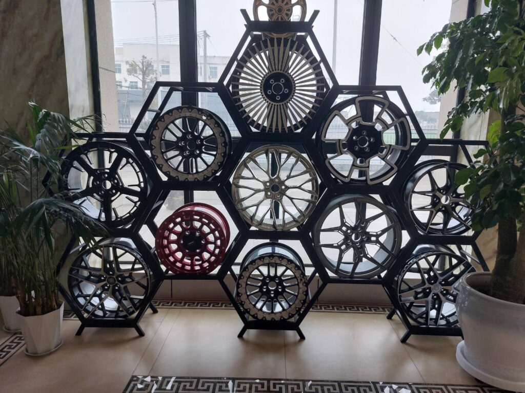 Display of various stylish alloy wheels arranged in a modern hexagonal rack near a window with greenery.